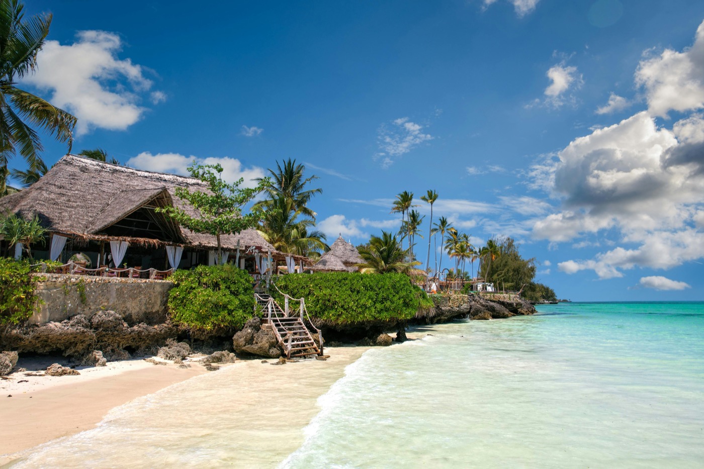 Thatched beach bungalows on white coral sand with turquoise Indian Ocean water in Zanzibar, Tanzania
